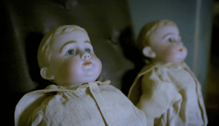 night time picture of two baby dolls with porcelain faces wearing vintage clothes and staring off to the side