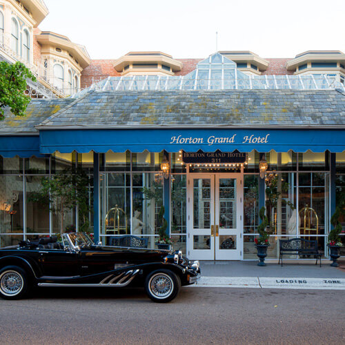 The glassed-in entrance to the Horton Grand Hotel in San Diego where a black vintage convertible automobile from the 1930s is parked near the loading zone