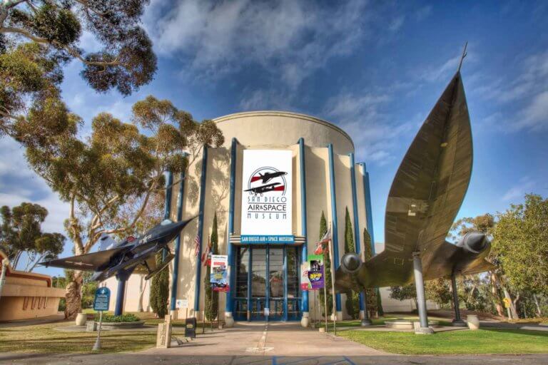 building exterior of San Diego Air & Space Museum with airplane models mounted on posts on either side of building