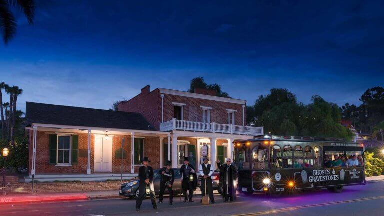 five san diego ghost hosts standing next to ghost trolley at night with the whaley house behind them