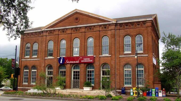 brick building exterior of Savannah History Museum with rows of windows rounded at the top and a sign that reads has an 'i' information symbol and the words 'Savannah Visitor Information'