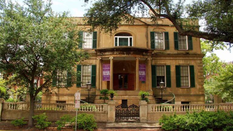 building exterior of owens thomas house in savannah, georgia featuring two staircases leading up to a columned entrance and four windows with shutters on either side