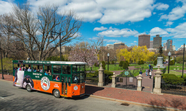 old town trolley in Boston driving past Boston Public Garden and George Washington Statue and city skyline in background