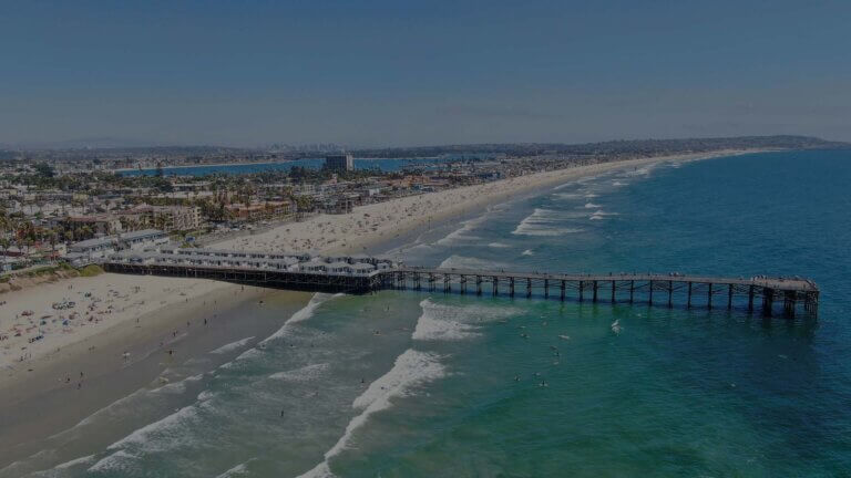 A vibrant view of San Diego's coastline, showcasing sandy beaches, palm trees, and the sparkling Pacific Ocean under a clear sky.